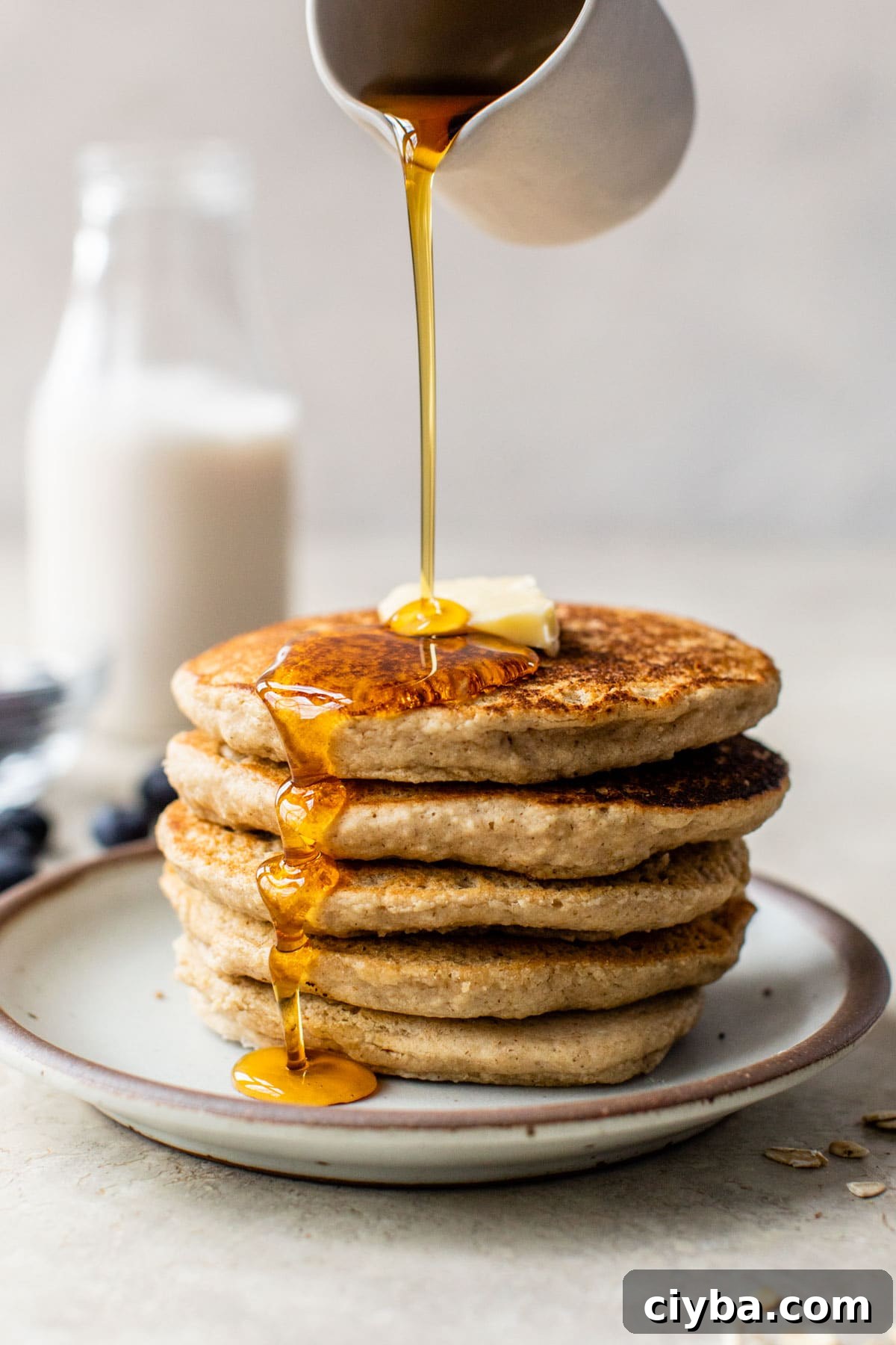 someone pouring maple syrup over a stack of pancakes