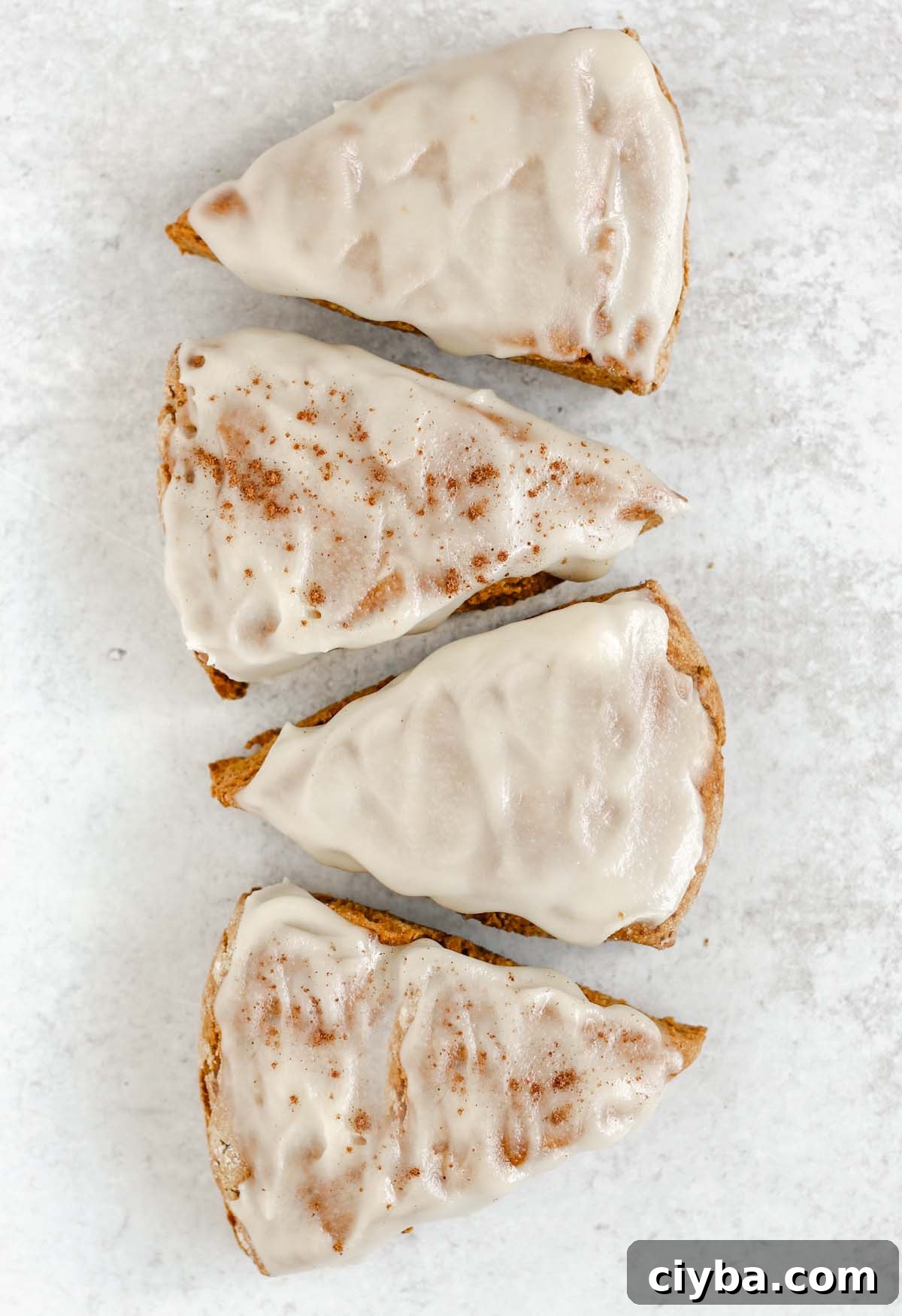 Four frosted pumpkin scones laid out in a line on a gray surface.