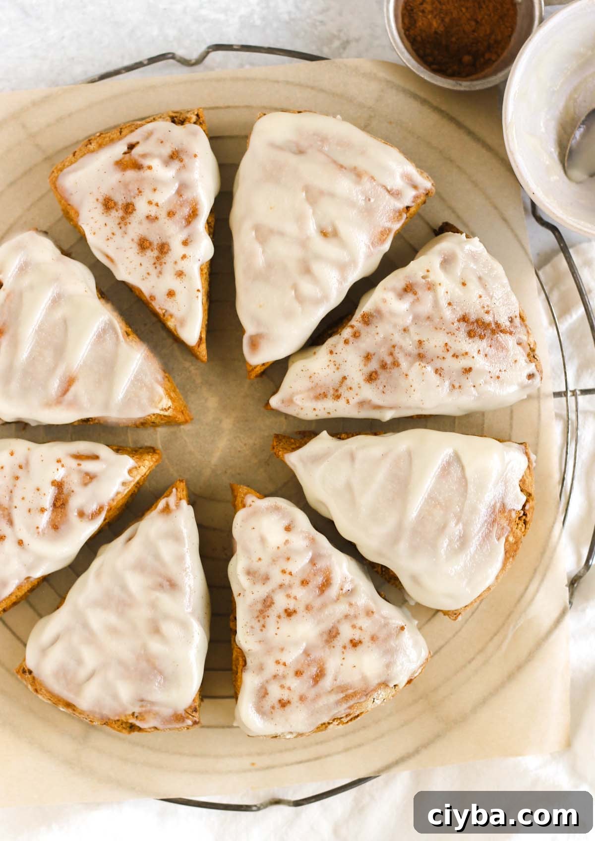 Eight frosted pumpkin scones on a round cooling rack.
