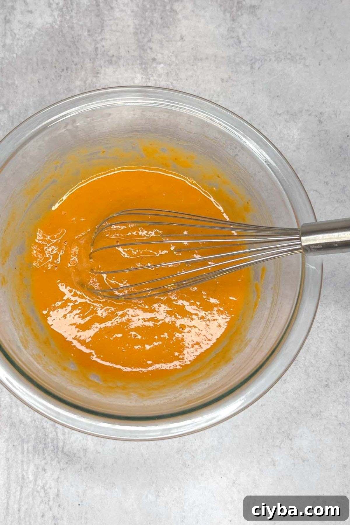 Wet ingredients for pumpkin scones with a whisk in a glass mixing bowl.