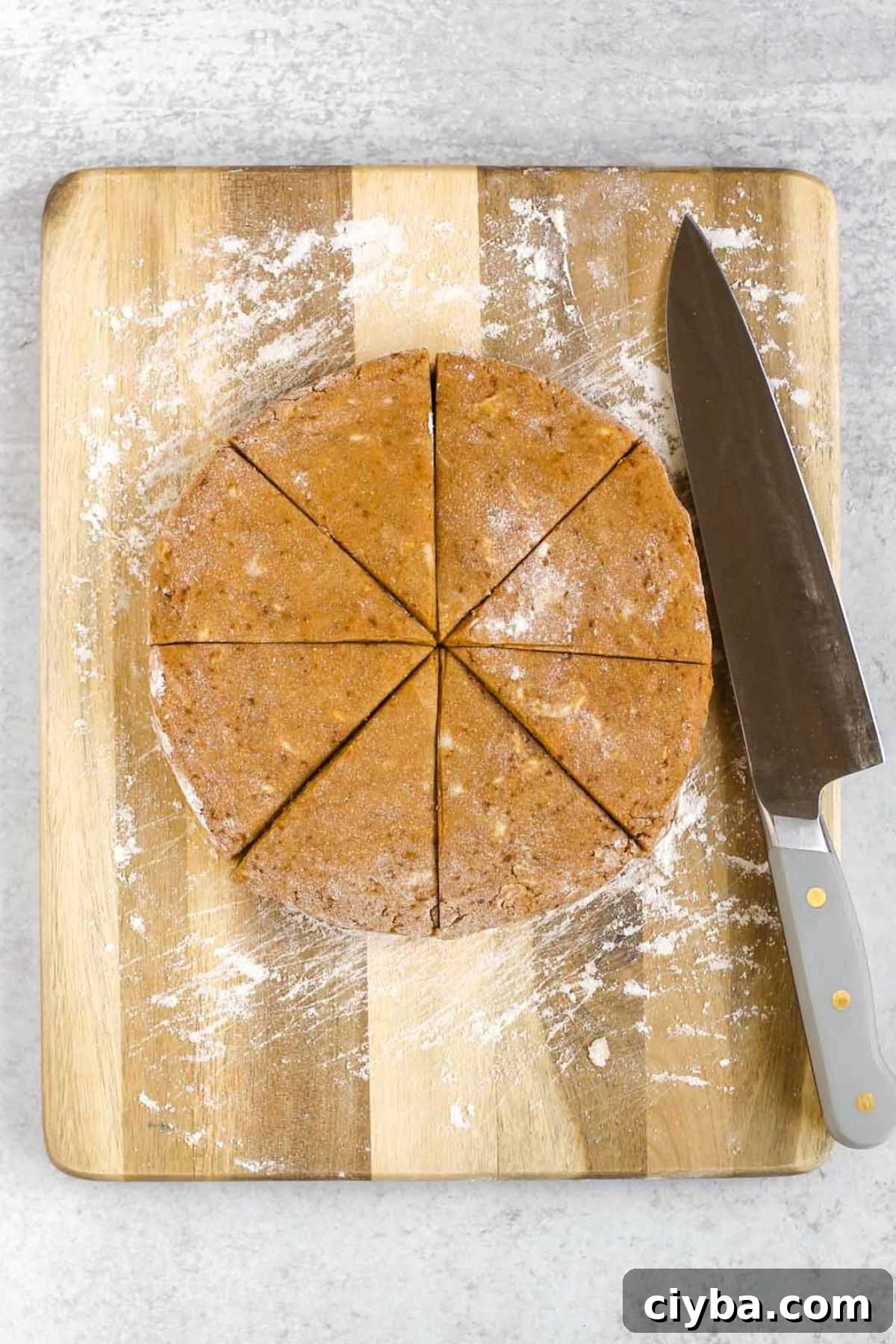 Pumpkin scone dough round cut into 8 wedges on a cutting board.