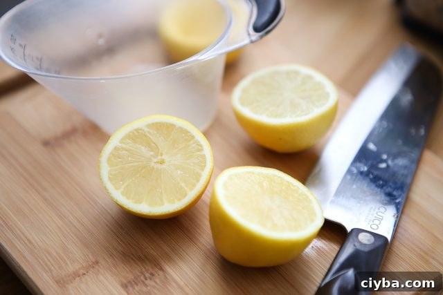 two lemons sliced in half on wooden cutting board with measuring cup and large knife