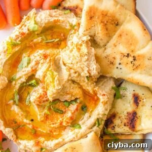 A triangle of pita being dipped into hummus that's sprinkled with parsley, paprika and drizzled with olive oil.