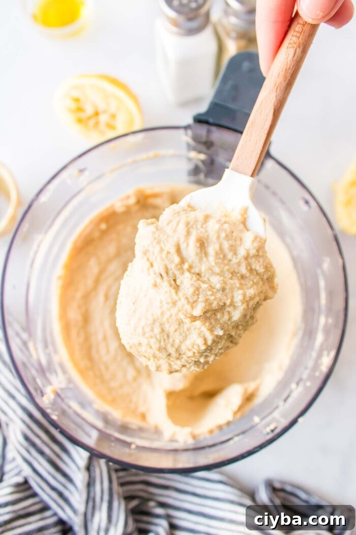 A hand holding a spatula with a large scoop of hummus on it.
