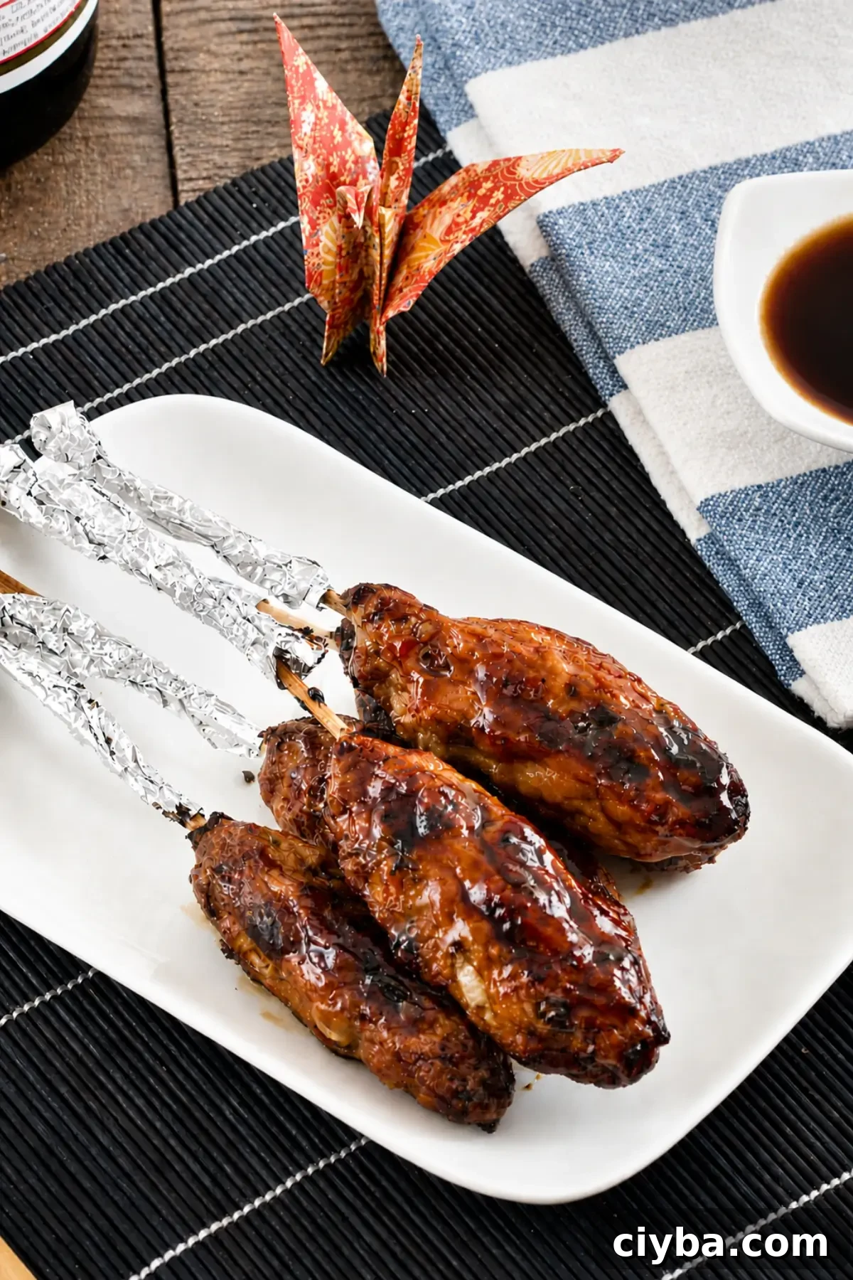 Yakitori-glazed chicken skewers with charred edges served with dipping sauce on a white platter.