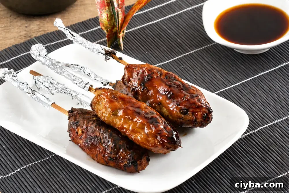Yakitori-glazed chicken skewers with charred edges served with dipping sauce on a white platter.
