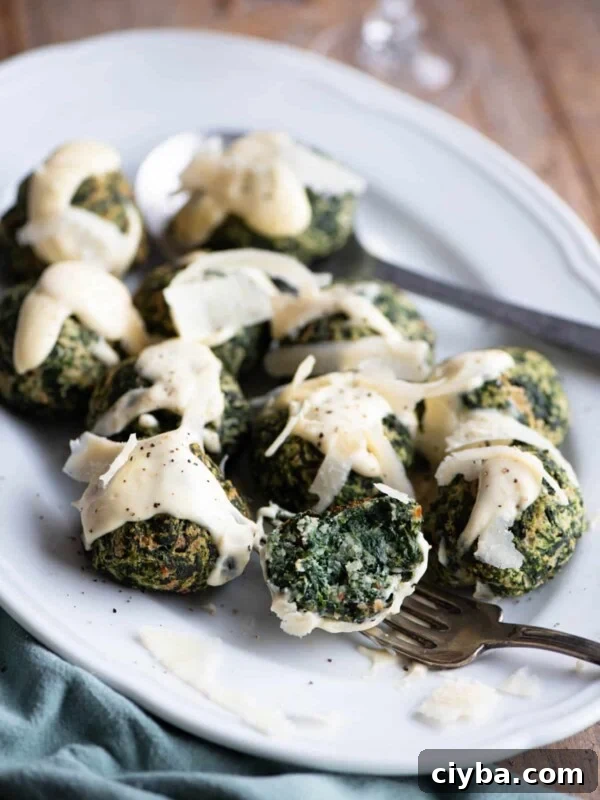 Spinach balls on a white serving plate with parmesan cream. One is cut open on a fork.