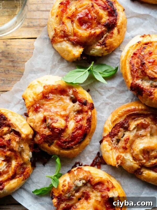 An overhead shot of pizza pinwheels on a wooden board with a basil leaf and glass of wine at the side.