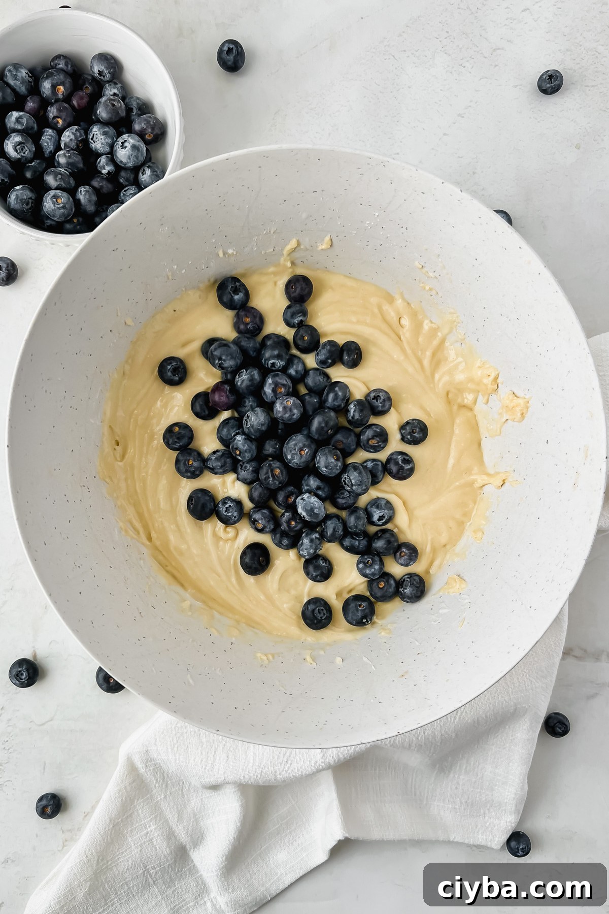 blueberry protein muffins batter mixed and topped with handful of fresh blueberries.
