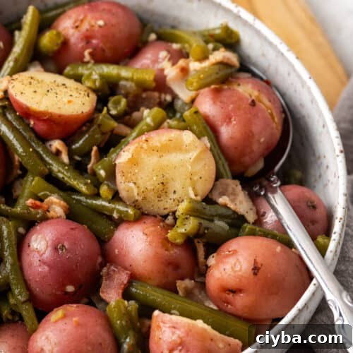 A serving dish of green beans and potatoes with bacon.