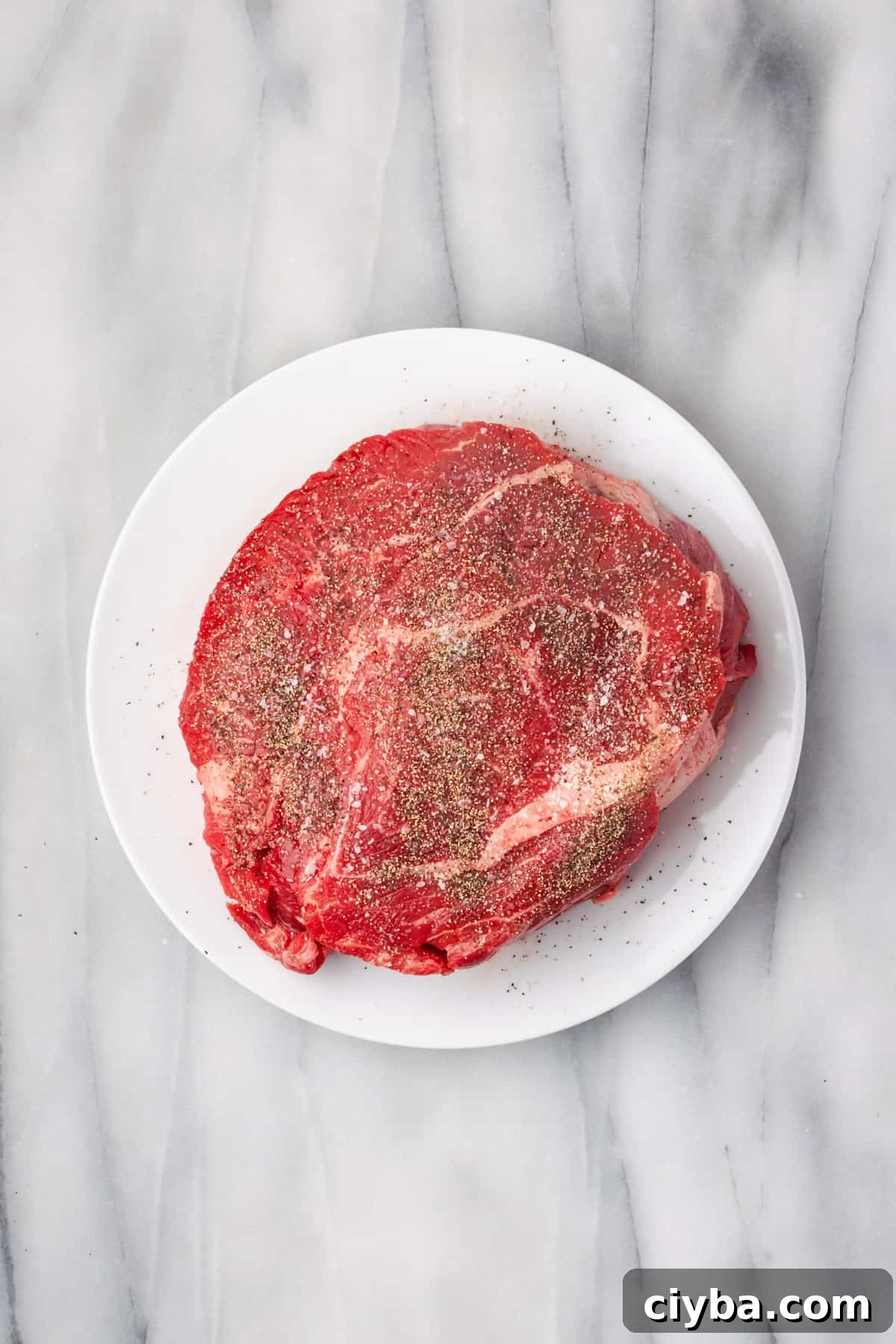 A piece of beef chuck roast dusted with salt and pepper sitting on a plate.