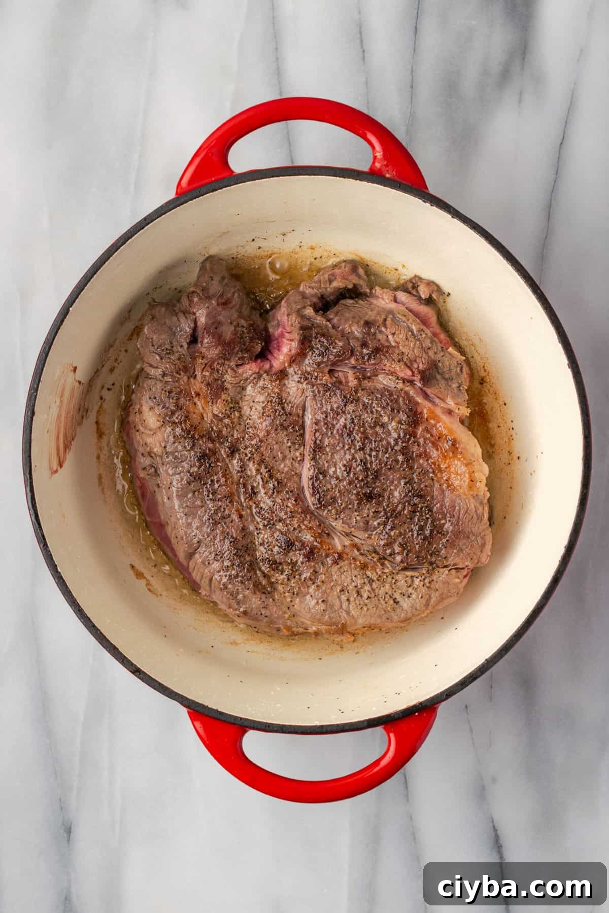 A browned chuck roast in a large Dutch oven pot. 