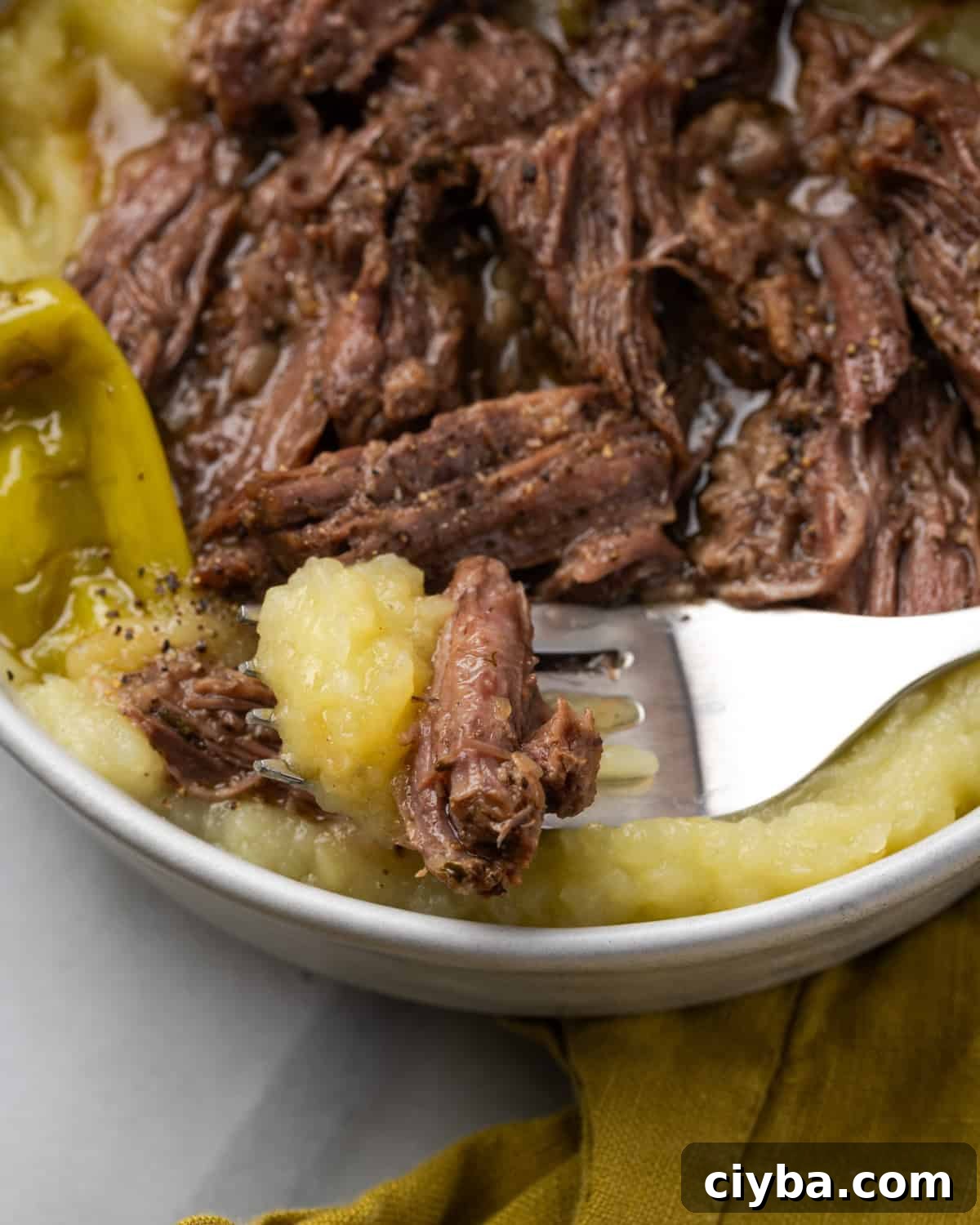 A fork scooping up a bite of mashed potatoes and pot roast.