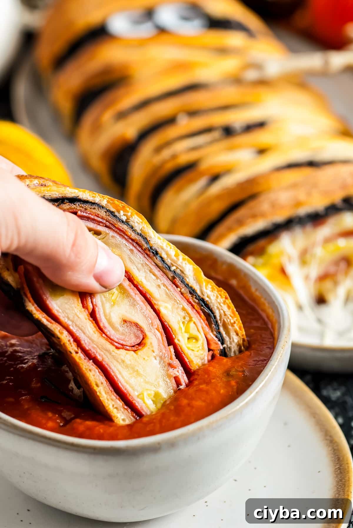 Hand dipping slice of the Stromboli into marinara sauce.