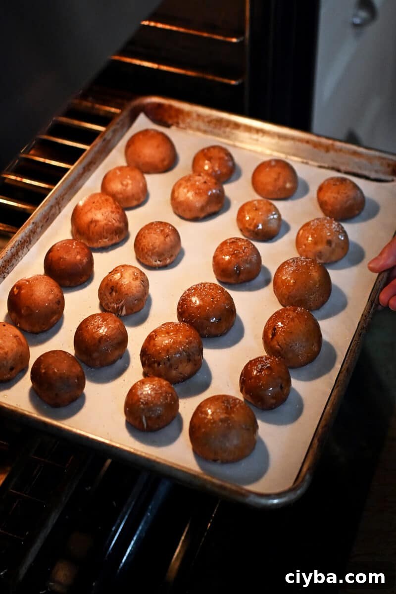 A baking sheet of cremini mushrooms (gill-side down) being placed into an oven.