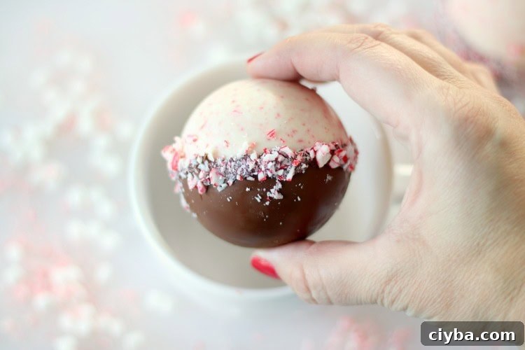 hand holding peppermint bark hot chocolate bomb over mug