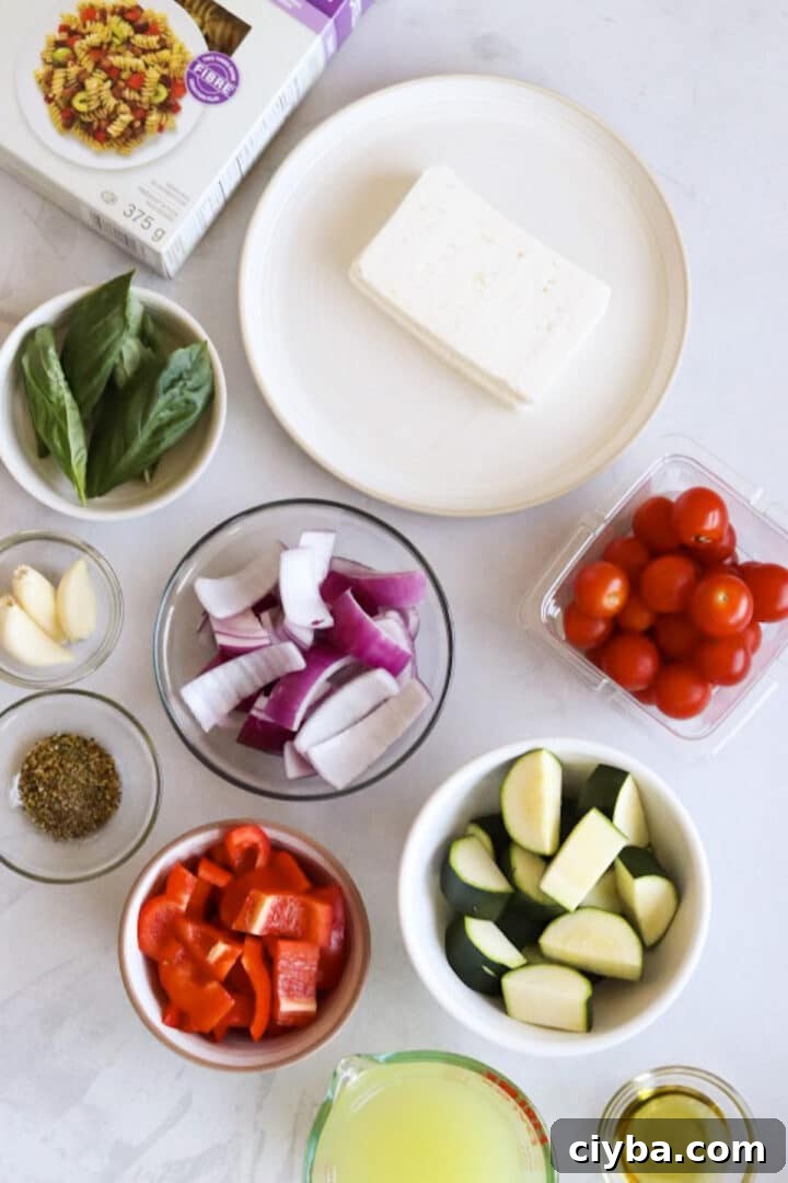 Ingredients for baked feta pasta with more vegetables displayed in small bowls on a white kitchen counter