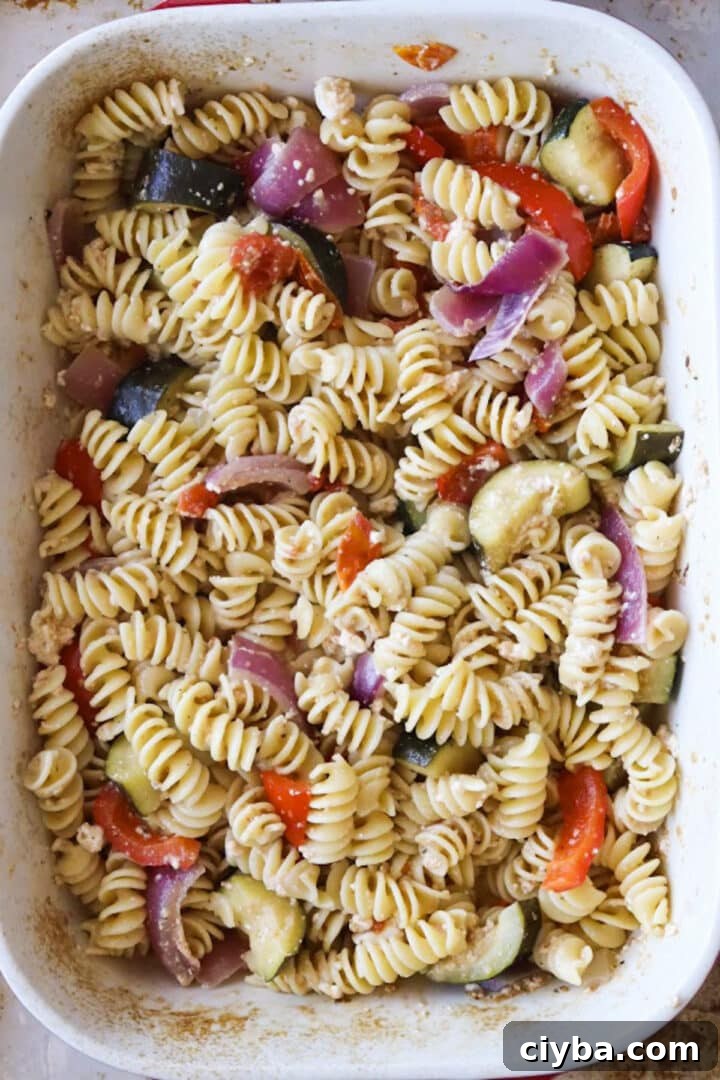 Stirred baked feta pasta with extra roasted vegetables in a large baking dish