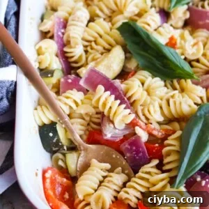 Baking pan with baked feta pasta with more vegetables prepared, topped with fresh basil
