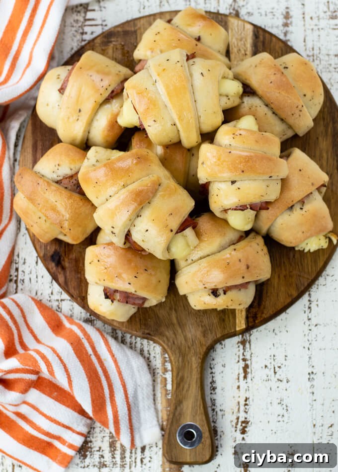 A platter of baked ham and cheese crescent rolls with an orange and striped dish towel beside it.