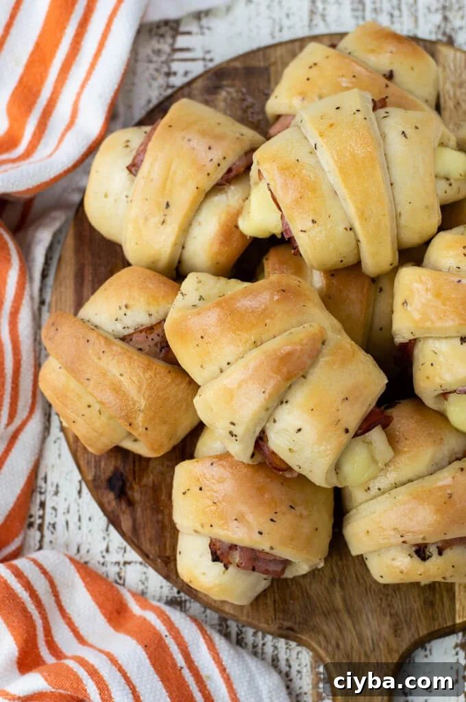 A platter of baked ham and cheese crescent rolls with an orange and striped dish towel beside it.