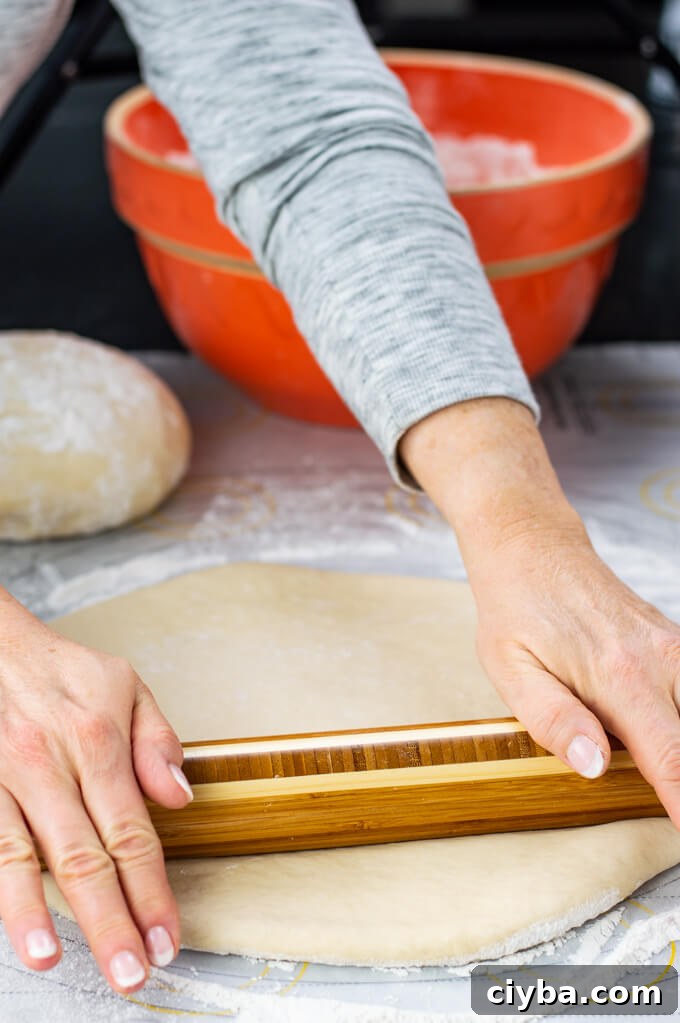 Rolling out dough with a rolling pin. A ball of dough and an orange mixing bowl sits in the background.