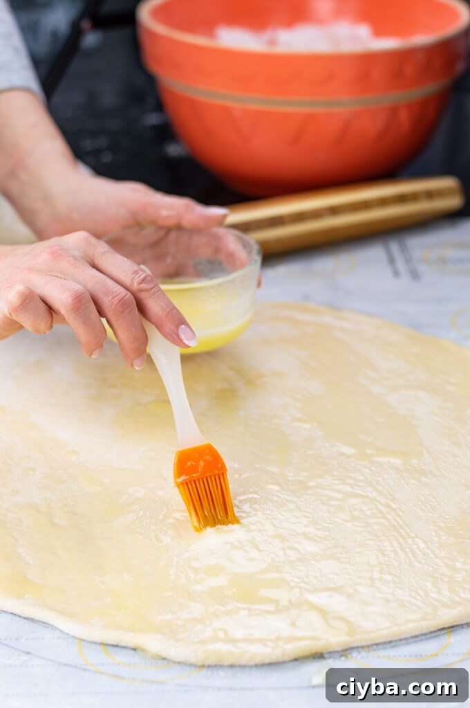 Brushing butter on rolled out dough. A rolling pin sits in the background with an orange mixing bowl.
