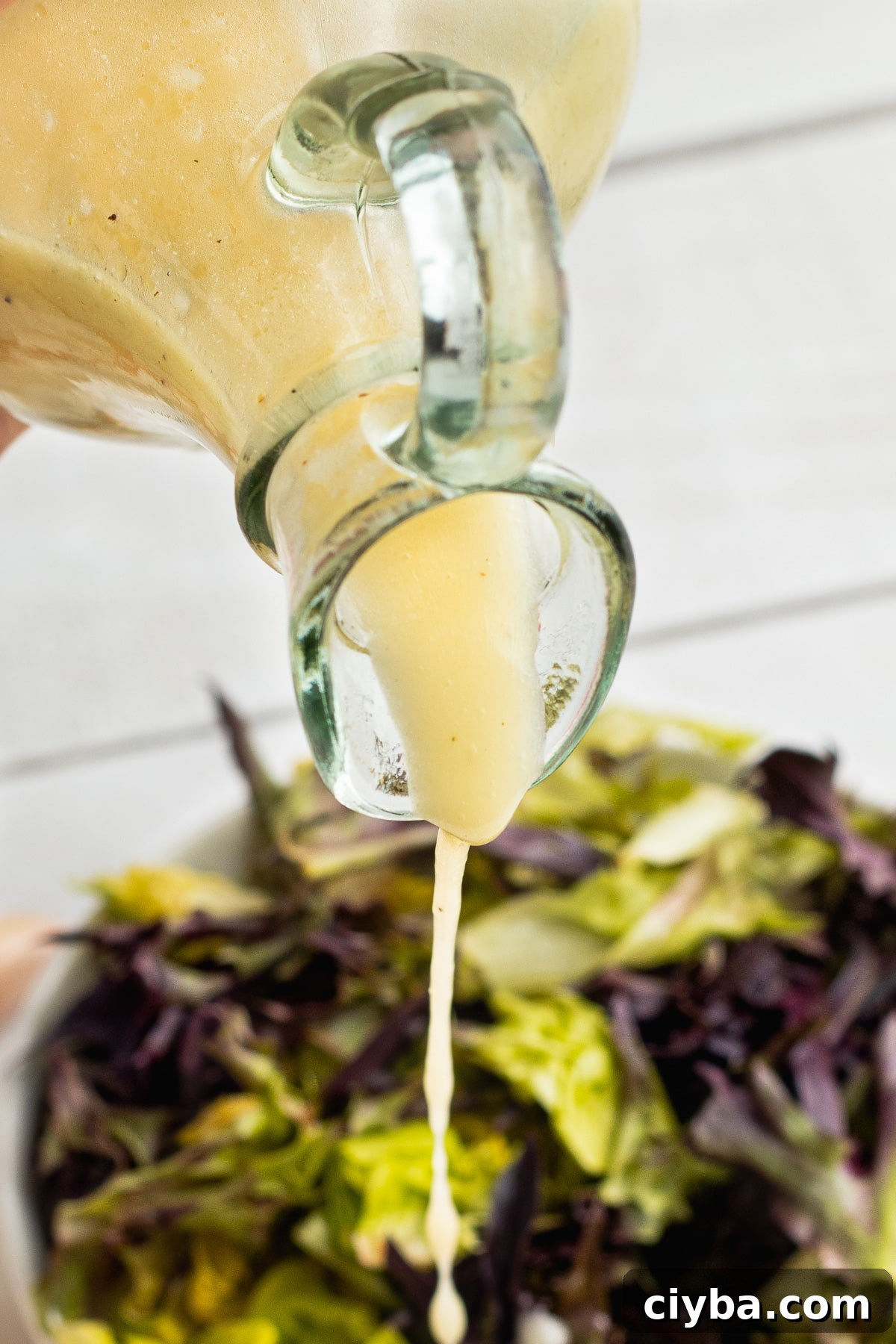 Picture of homemade vinaigrette being poured over a salad.
