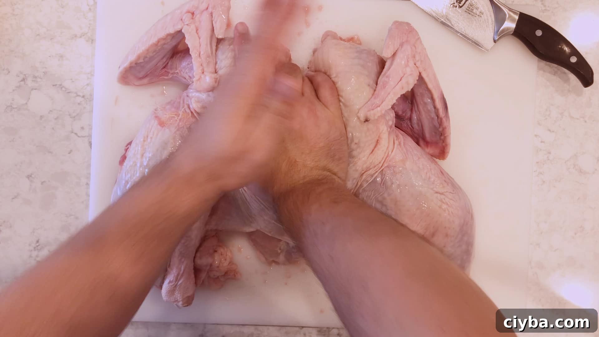 Hands pressing down on a spatchcocked turkey