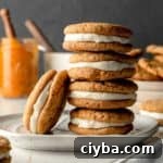 A stack of pumpkin cream pies, one cookie leaning against the stack. Pumpkin puree and a frosting bowl in the background.