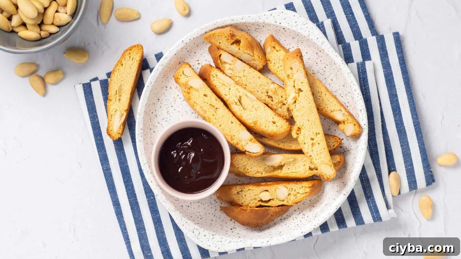 A plate of almond biscotti with a small bowl of chocolate sauce on a blue and white striped cloth. Almonds are scattered around.