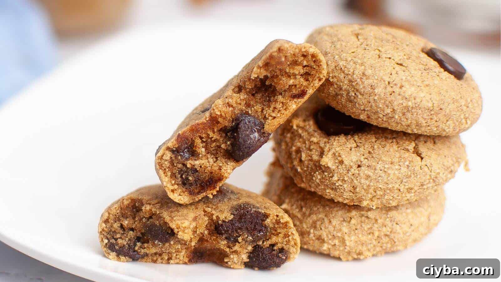 A stack of chocolate chip cookies on a white plate, with one cookie broken in half to show the chocolate chips inside.
