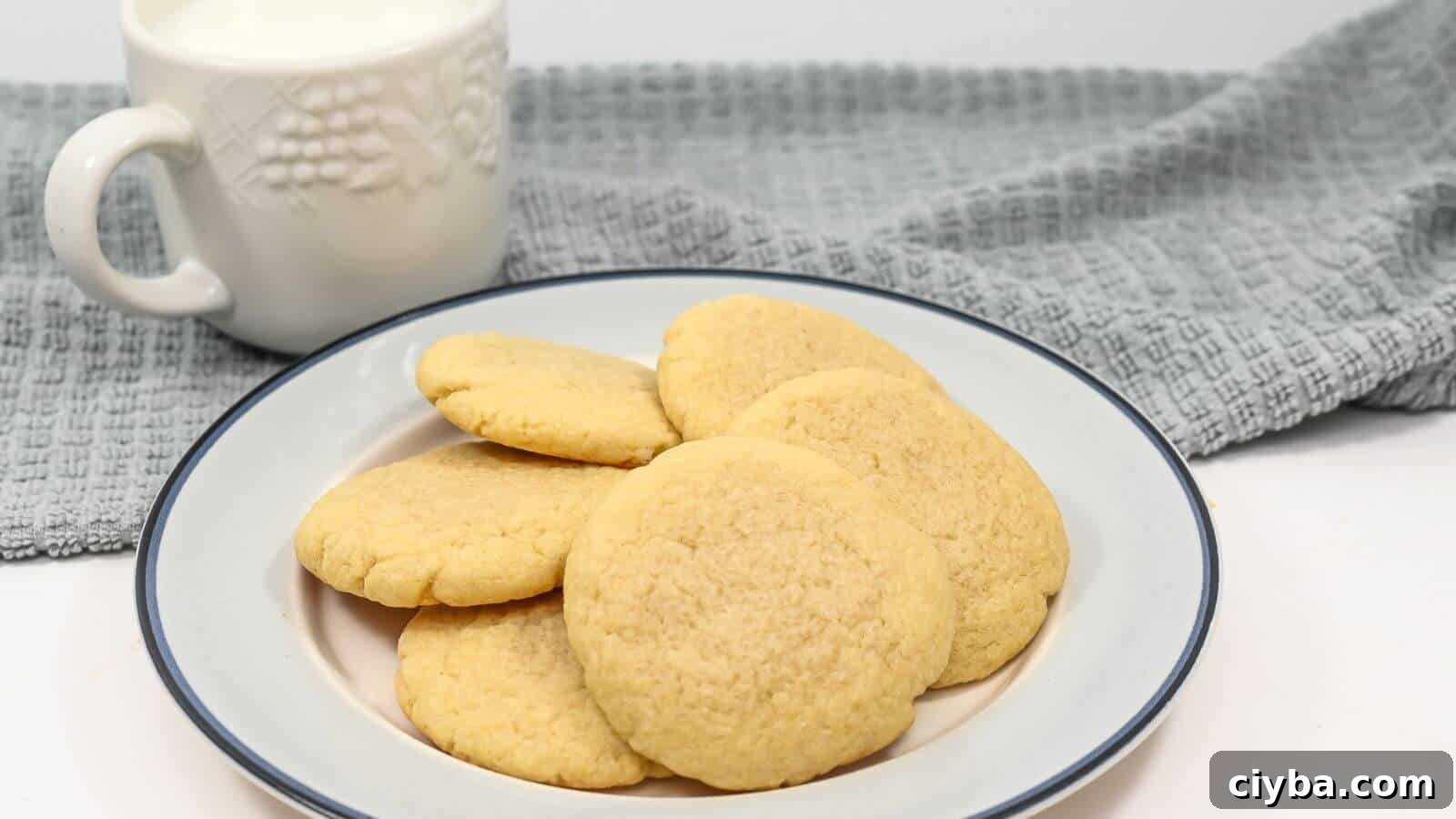 A plate of sugar cookies with a mug of milk and a gray cloth in the background.