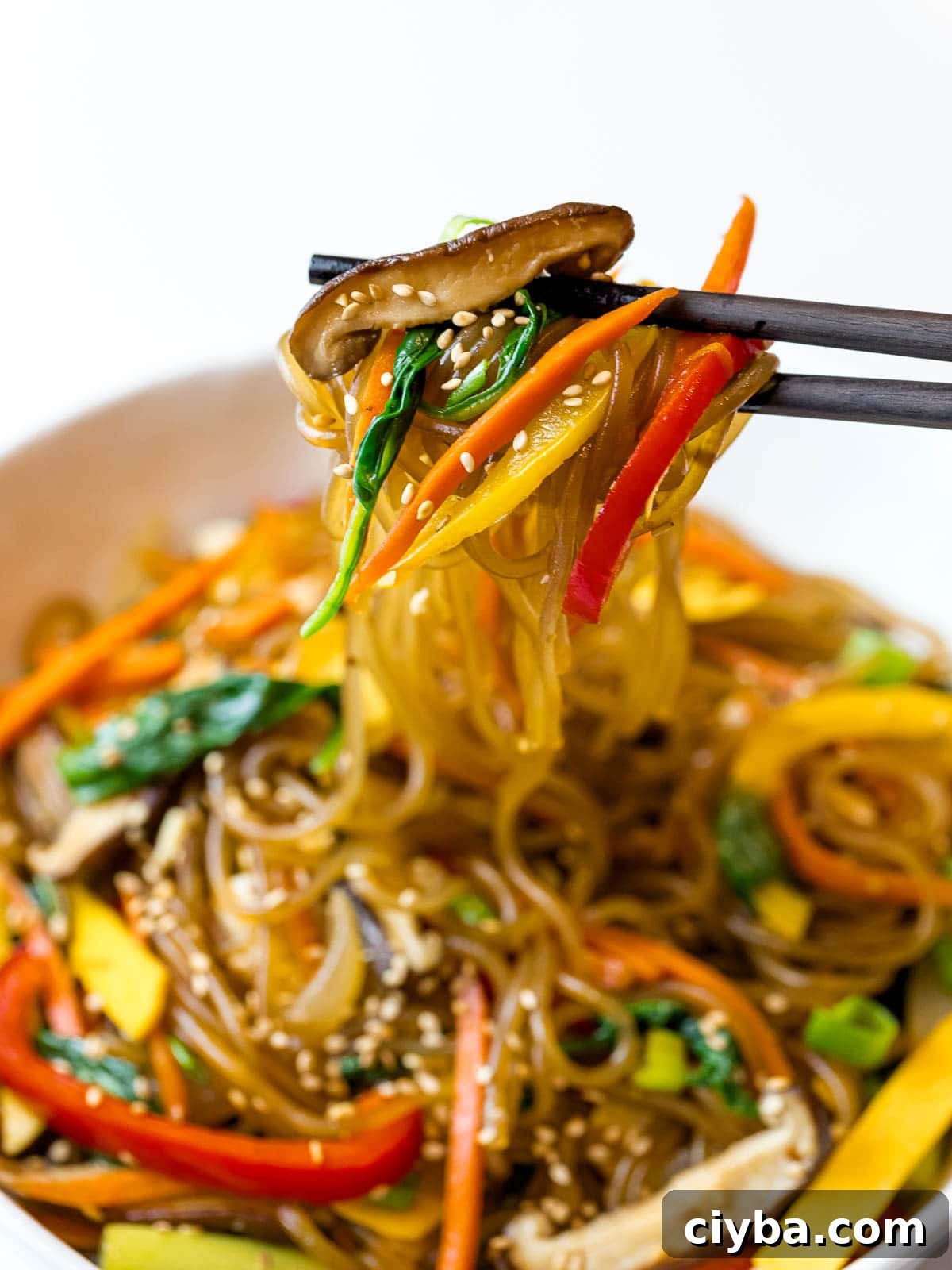 Authentic Japchae: Korean Glass Noodle Stir Fry Recipe 14 close up of Korean japchae noodles with stir fried vegetables picked up by chopsticks