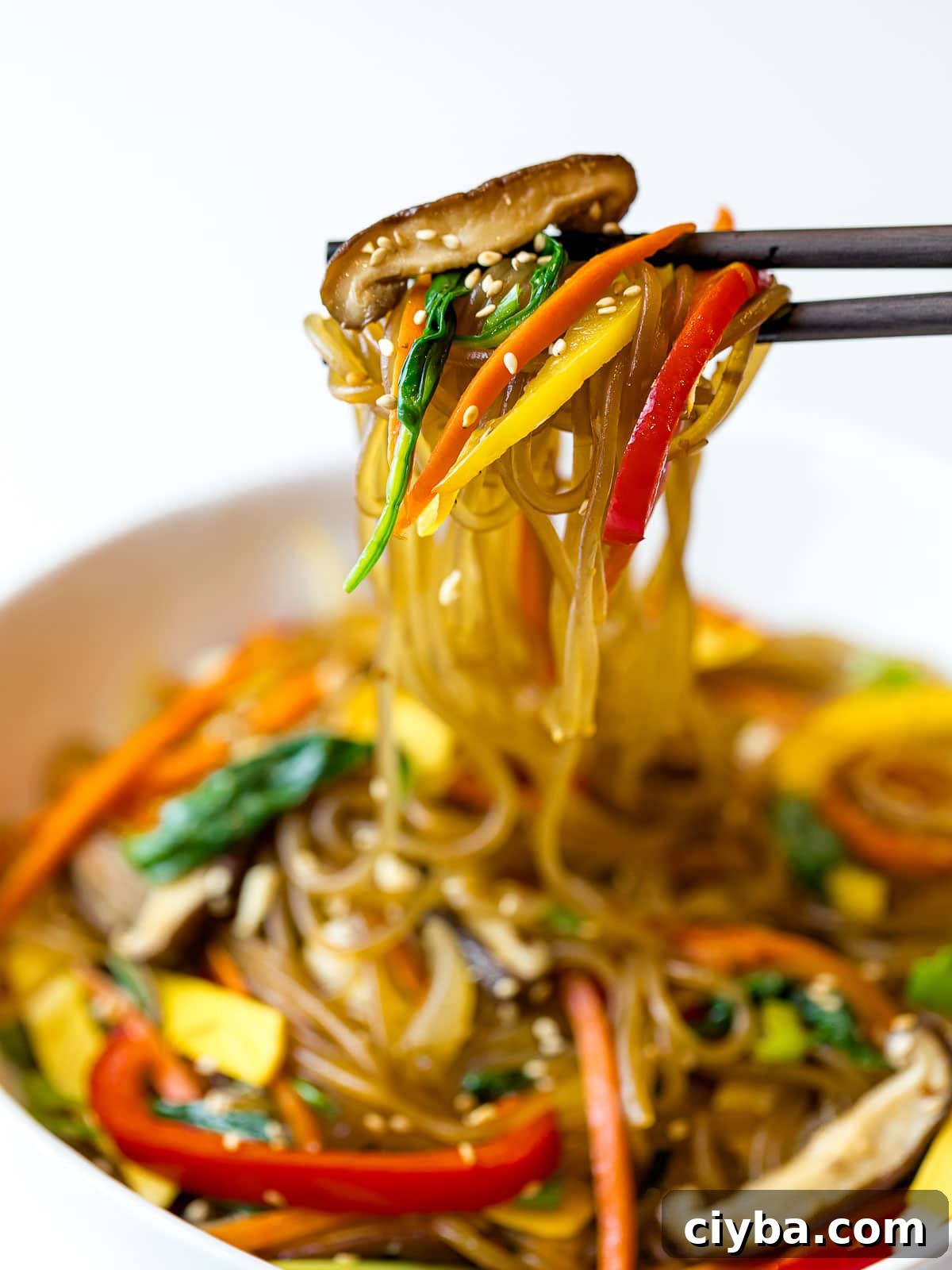 Authentic Japchae: Korean Glass Noodle Stir Fry Recipe 3 japchae glass noodles with colorful vegetables held up by chopsticks