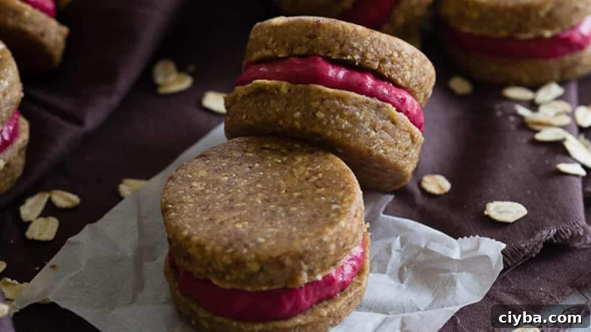 oatmeal sandwich cookies with raspberry filling on a dark cloth with parchment paper.