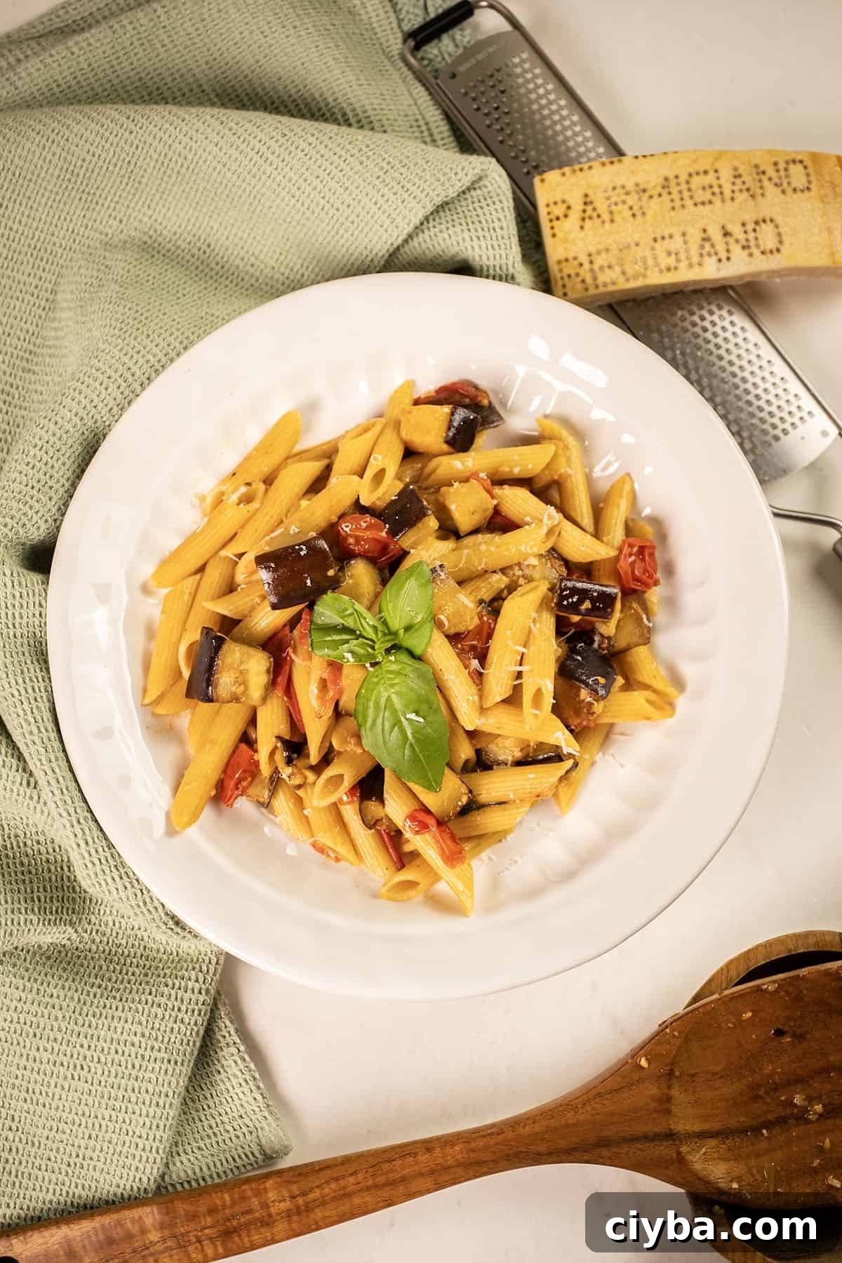 Pasta with eggplant and cherry tomatoes in a bowl garnished with fresh basil.
