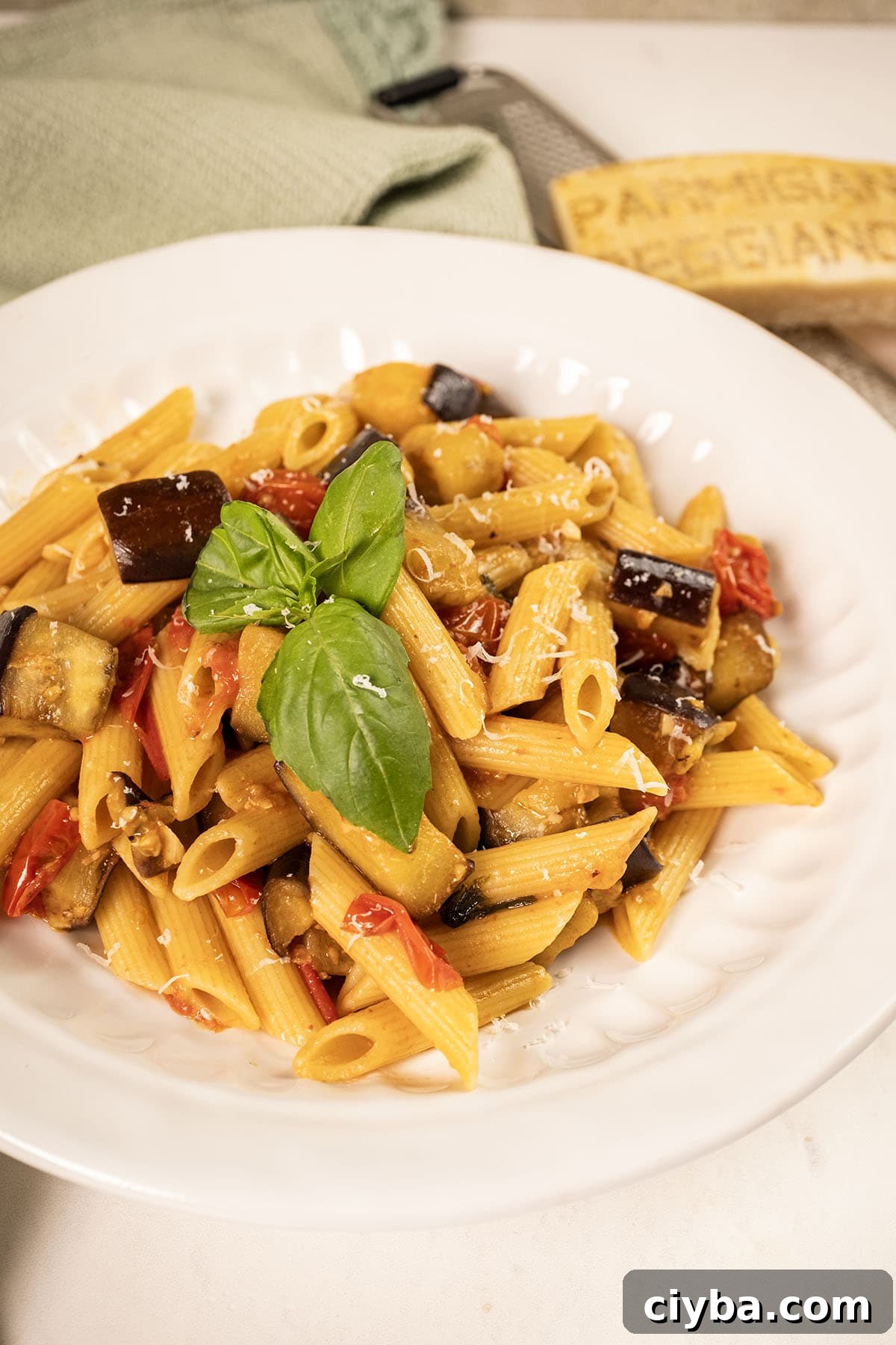 Pasta with eggplant and cherry tomatoes in a bowl garnished with fresh basil.