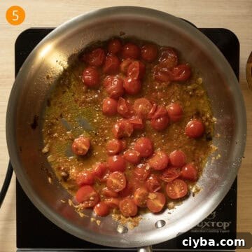 Cherry tomatoes breaking down in a pan and wine sauce thickening.