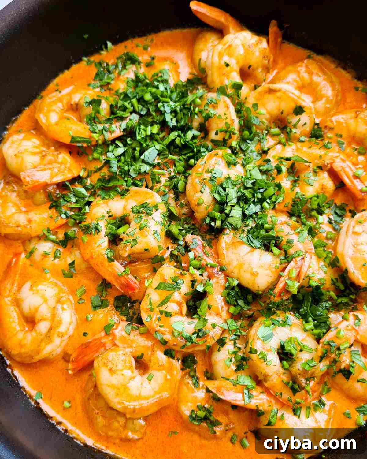 Creamy garlic shrimp (prawns) topped with finely chopped fresh parsley in a frying pan