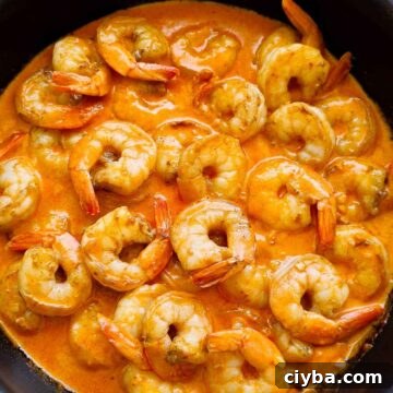 Close up of shrimp in creamy sauce topped with parsley in a pan with a spoon