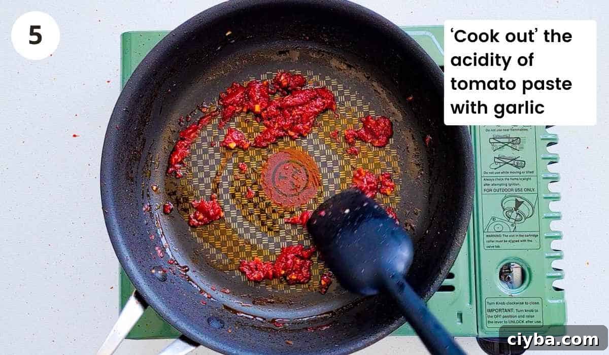 Tomato paste with garlic being cooked in a frying pan with caption
