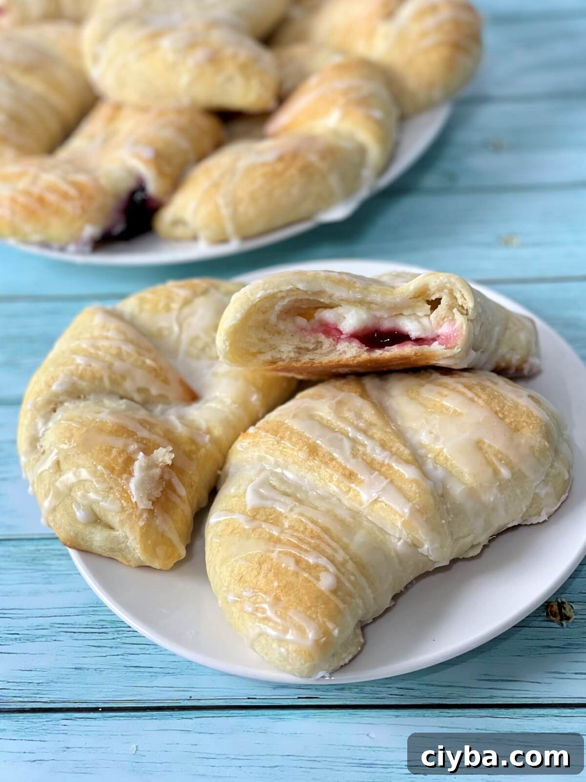 A closeup of soft cream cheese danish pastries, one open with the cream cheese and cherry filling showing on the inside.
