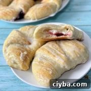 A closeup of soft cream cheese danish pastries, one open with the cream cheese and cherry filling showing on the inside.