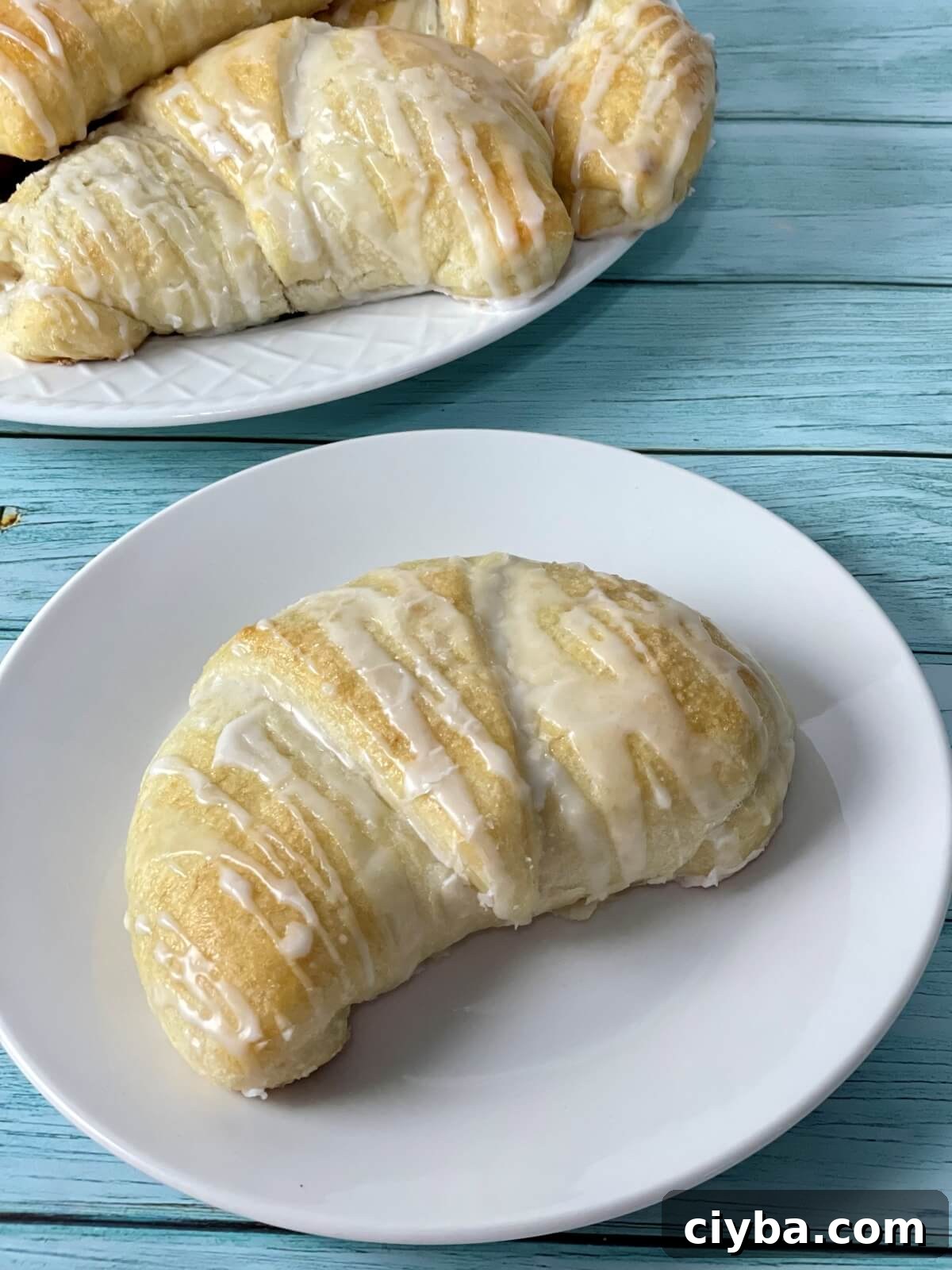 A plate with a large fluffy cream cheese danish on it, with more soft danishes pictured in the background.