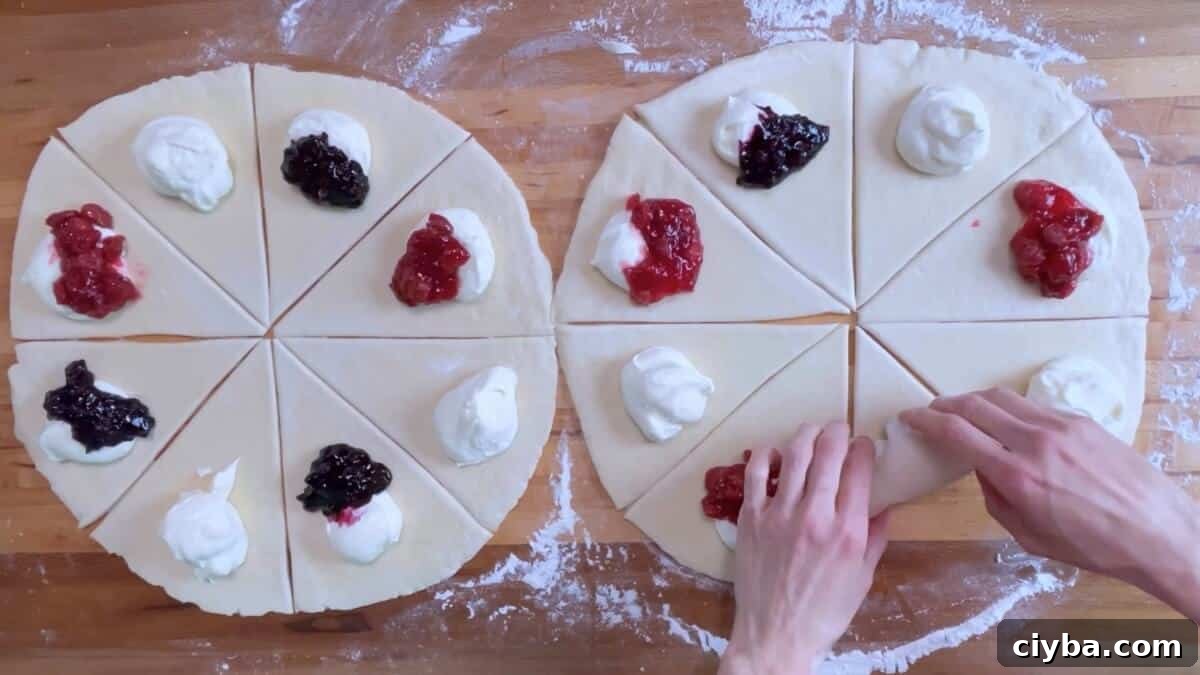 Two circles of rolled out danish dough cut into 8 triangles each, topped with cream cheese filling, cherry filling, and blueberry filling.