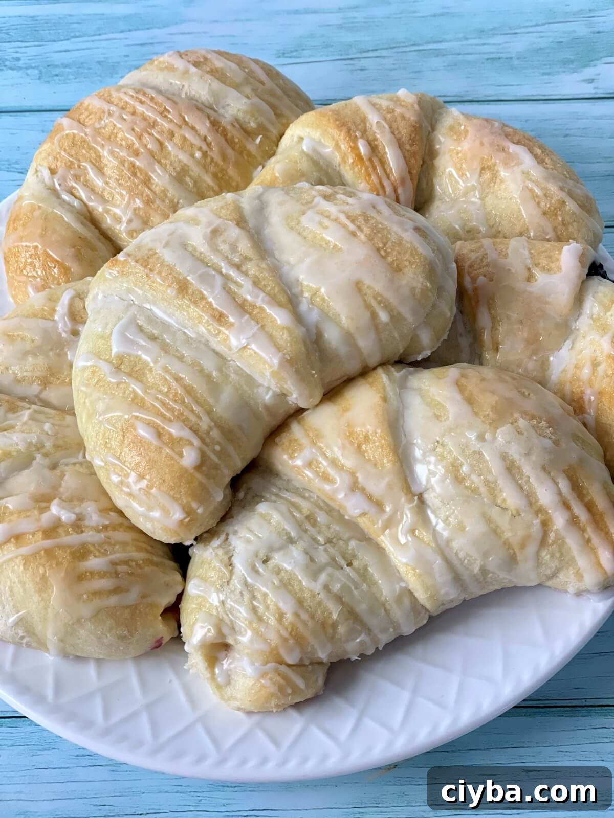 A closeup of a plate of large soft and fluffy cheese danish with glaze.