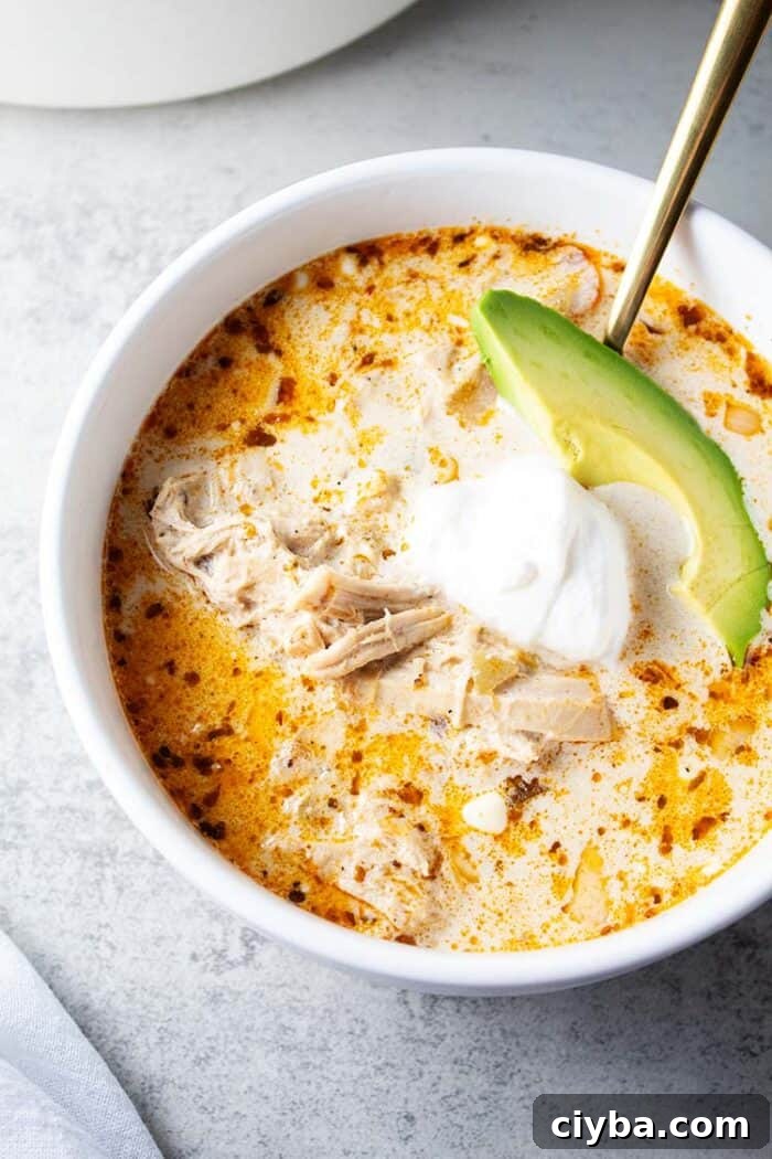 Keto Super Bowl Party Menu: Low-Carb Game Day Recipes 26 overhead view of bowl of keto white chicken chili in white serving bowl and gold serving spoon and garnished with slice of avocado and sour cream