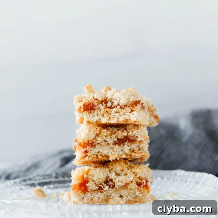 Three stacked coconut peach crumb bars on a cut glass plate with a dark grey napkin in the background.