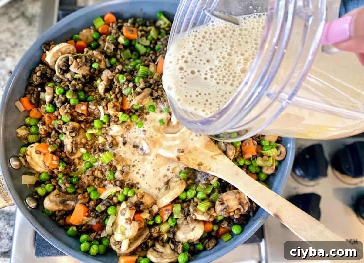 Hearty Vegan Shepherd's Pie with Lentils and Mushrooms 7 I am pouring the plant milk mixture into the cooking cottage pie, lentil, and vegetable mixture.
